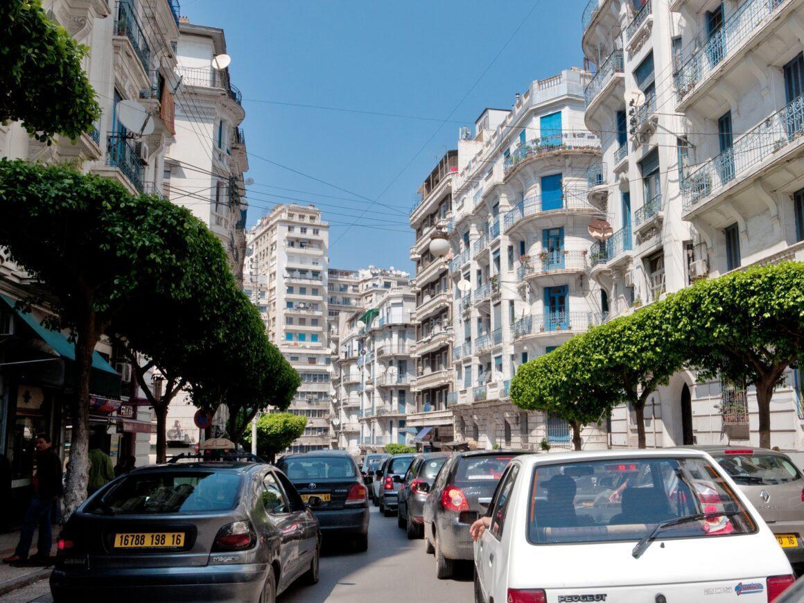 Busy street scene with cars and trees, featuring tall buildings under a clear blue sky.